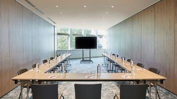 A conference room with a long table, chairs, a TV screen, and a projector stand.