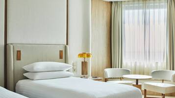 Ein Hotelzimmer mit einem großen Bett, zwei Sesseln, einem kleinen Tisch, einer Lampe und einem Fenster mit Vorhängen.