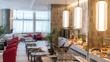A modern dining area with round tables, red chairs, and a buffet with various food items.