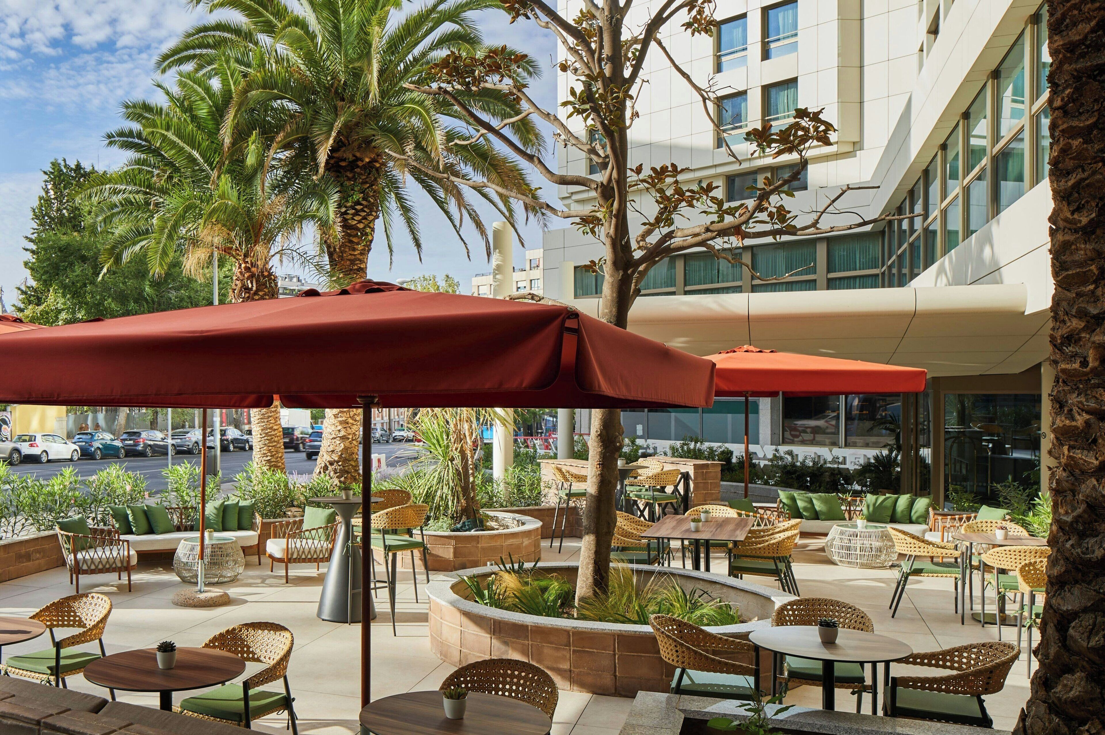 An outdoor seating area with wicker furniture, palm trees, and a red umbrella.