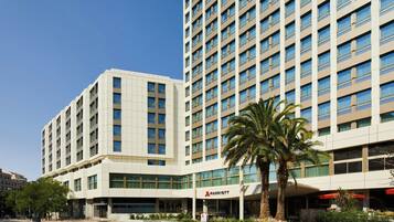 Un hotel de varios pisos con diseño moderno, que destaca un cartel grande de 'Marriott', amplias ventanas y una palmera en primer plano.