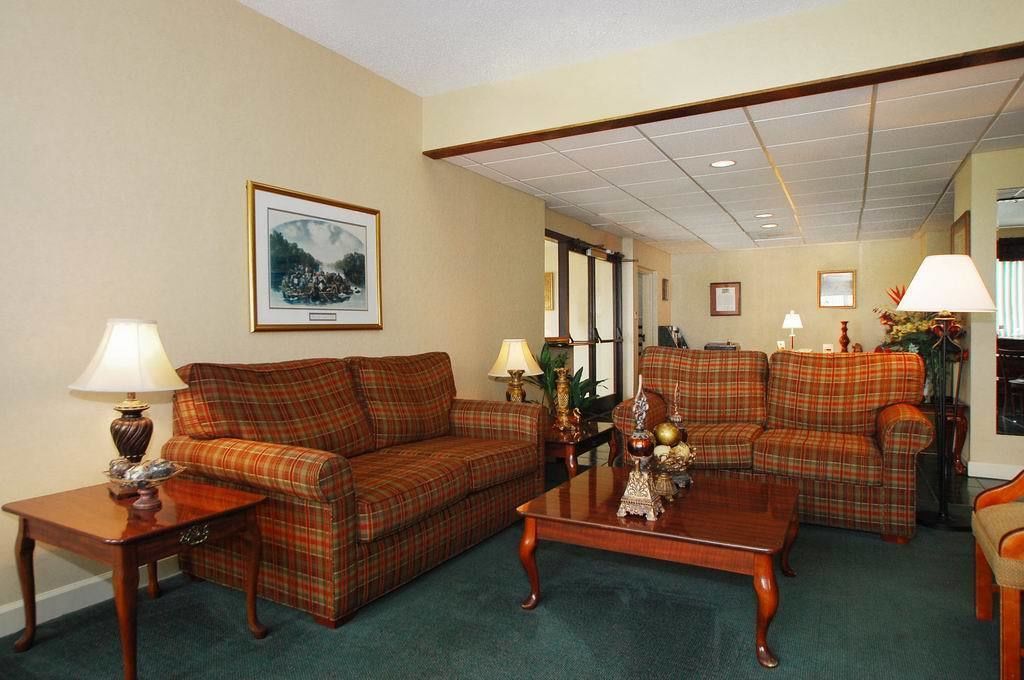 A living room with two plaid sofas, a coffee table, and lamps. There is a framed picture on the wall and a door leading to another room.