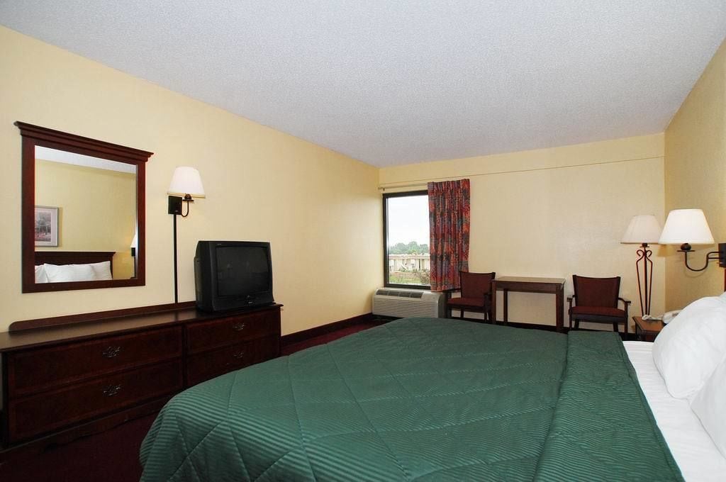 A hotel room with a bed, a desk, a television, a mirror, and a window with curtains.