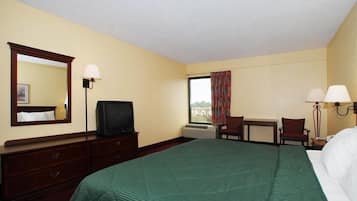 A hotel room with a bed, a desk, a television, a mirror, and a window with curtains.