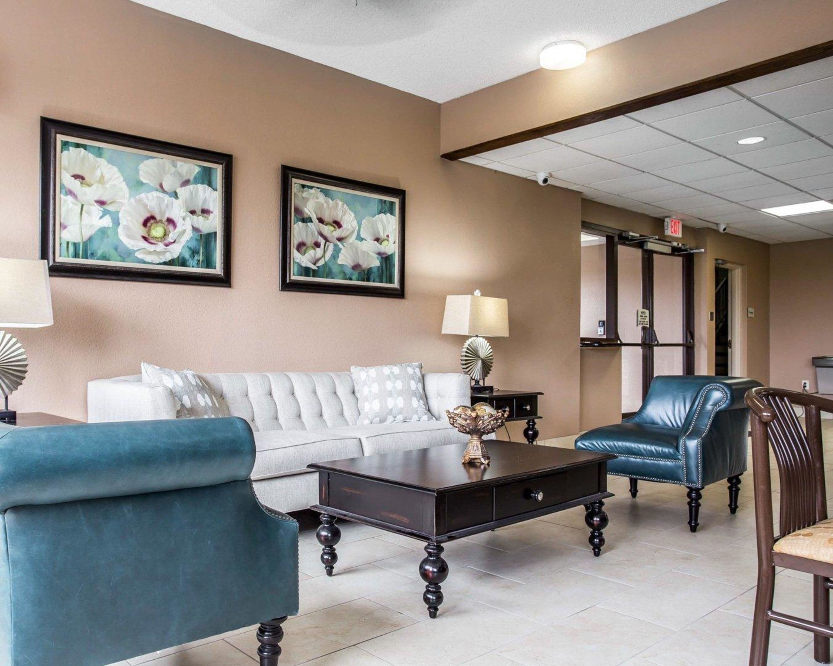 A lobby with a white sofa, a blue armchair, a dark wooden coffee table, and two framed floral paintings on the wall.