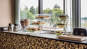 A breakfast buffet with multiple serving dishes and a coffee station by a window with a view of trees. - Quality Inn Mullins - Marion (Marion)