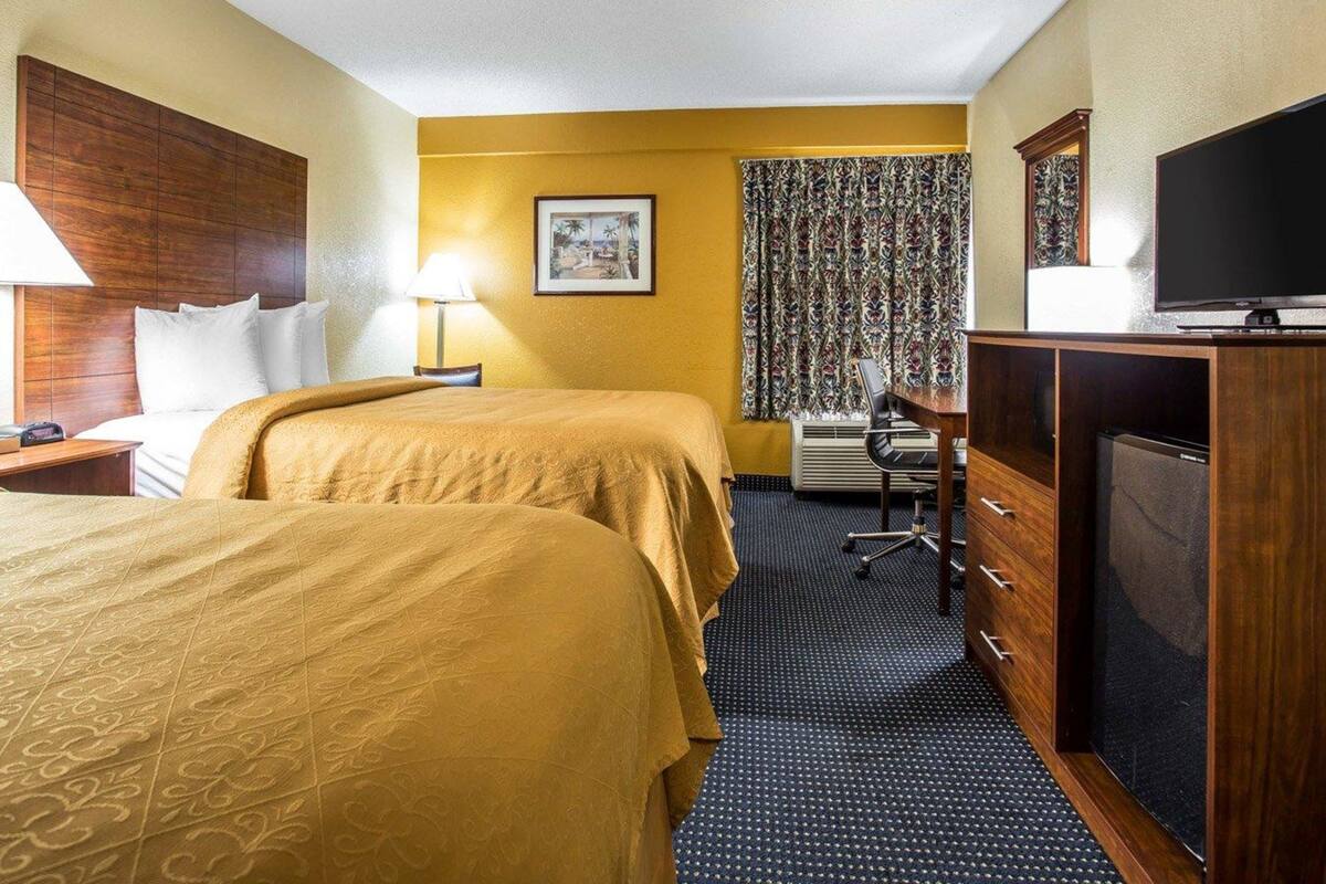 A hotel room with two beds, a desk, a chair, a television, and a wardrobe.