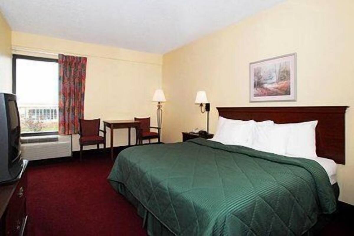 A hotel room with a bed, a desk, a chair, a television, and a window with curtains.
