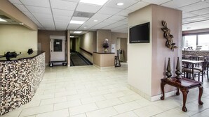 A hotel lobby with a reception desk, a wall-mounted TV, a decorative wall piece, and a seating area with tables and chairs. - Quality Inn Mullins - Marion (Marion)
