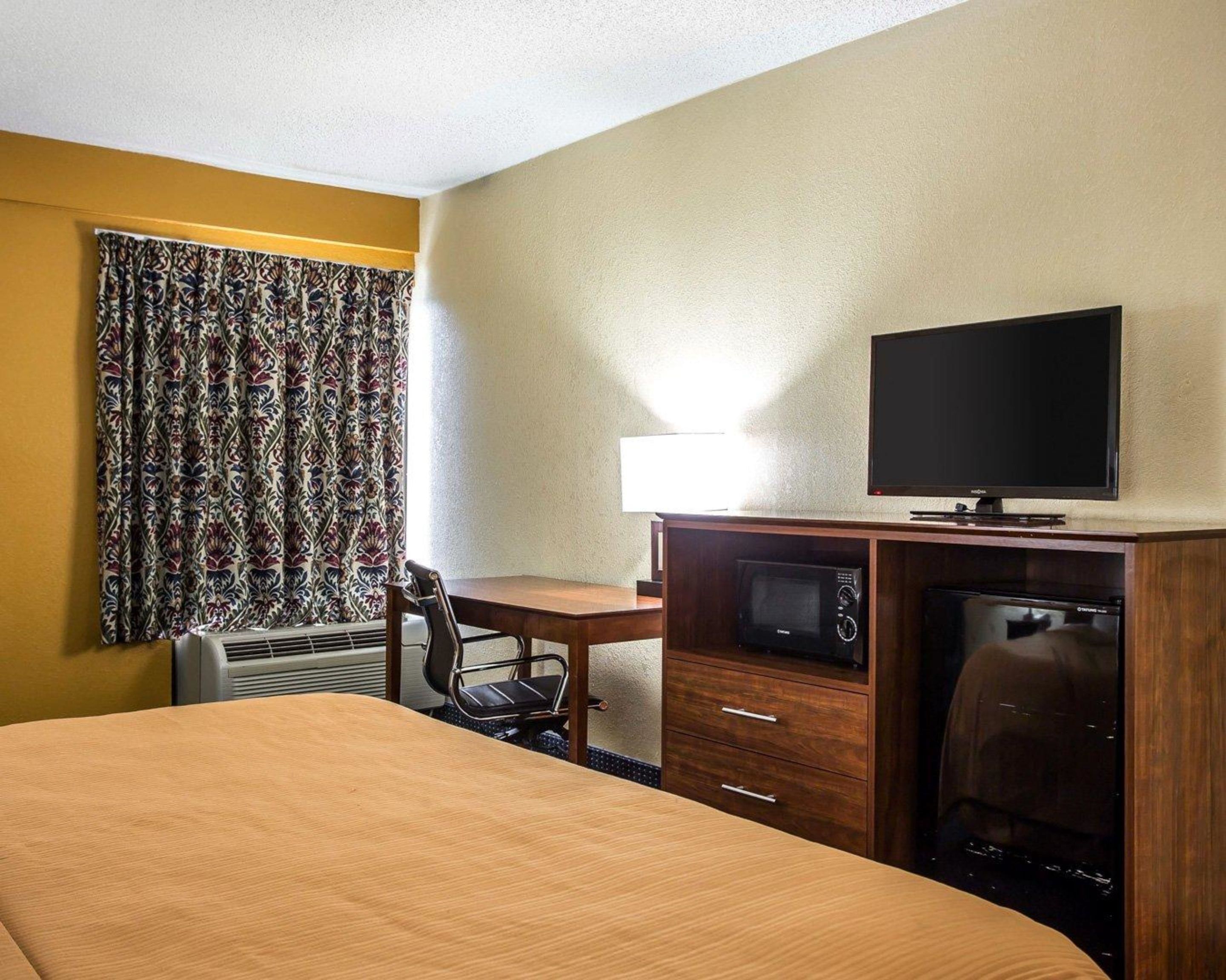A hotel room with a bed, a desk, a television, a microwave, and a refrigerator.