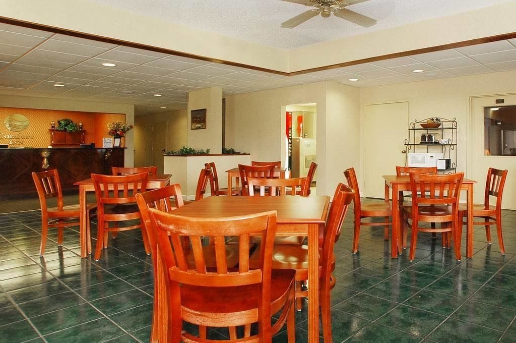 Une salle à manger d’hôtel avec des tables et des chaises en bois, un comptoir de réception et un ventilateur de plafond.