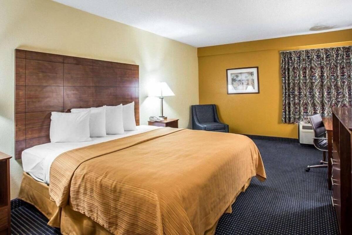 A hotel room with a large bed, a desk, a chair, a lamp, and a picture on the wall.