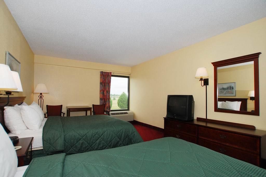 A hotel room with two beds, a television, a desk, and a window with curtains.