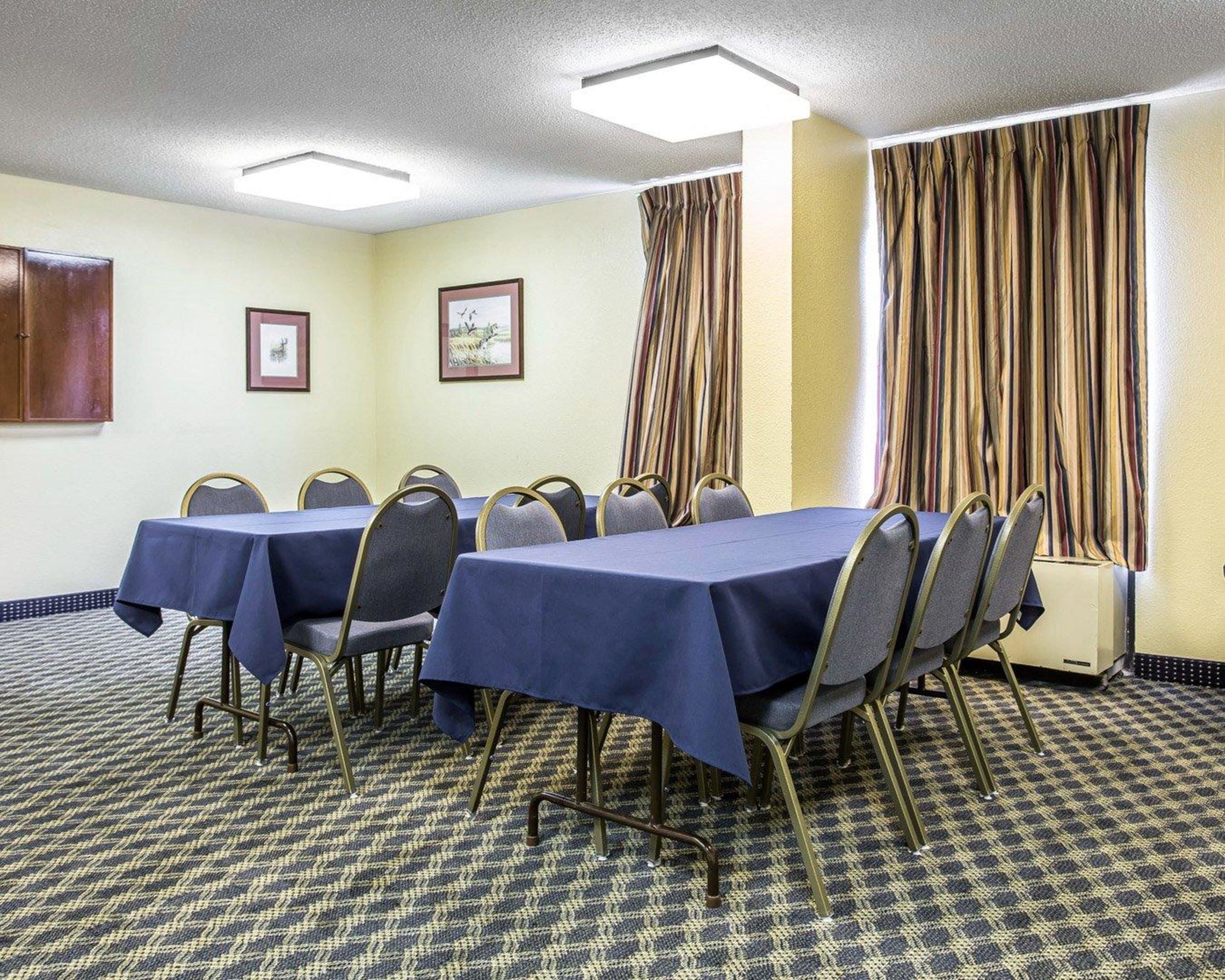 A conference room with a table set for meetings, chairs, framed pictures on the wall, and a window with curtains.