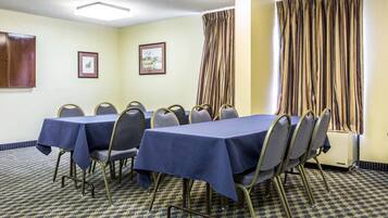 A conference room with a table set for meetings, chairs, framed pictures on the wall, and a window with curtains.