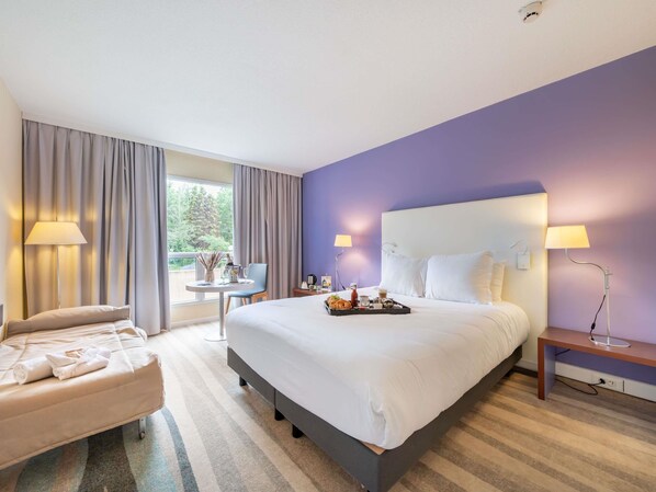 Une chambre d’hôtel avec un grand lit, un bureau, une chaise et une vue sur l’extérieur.