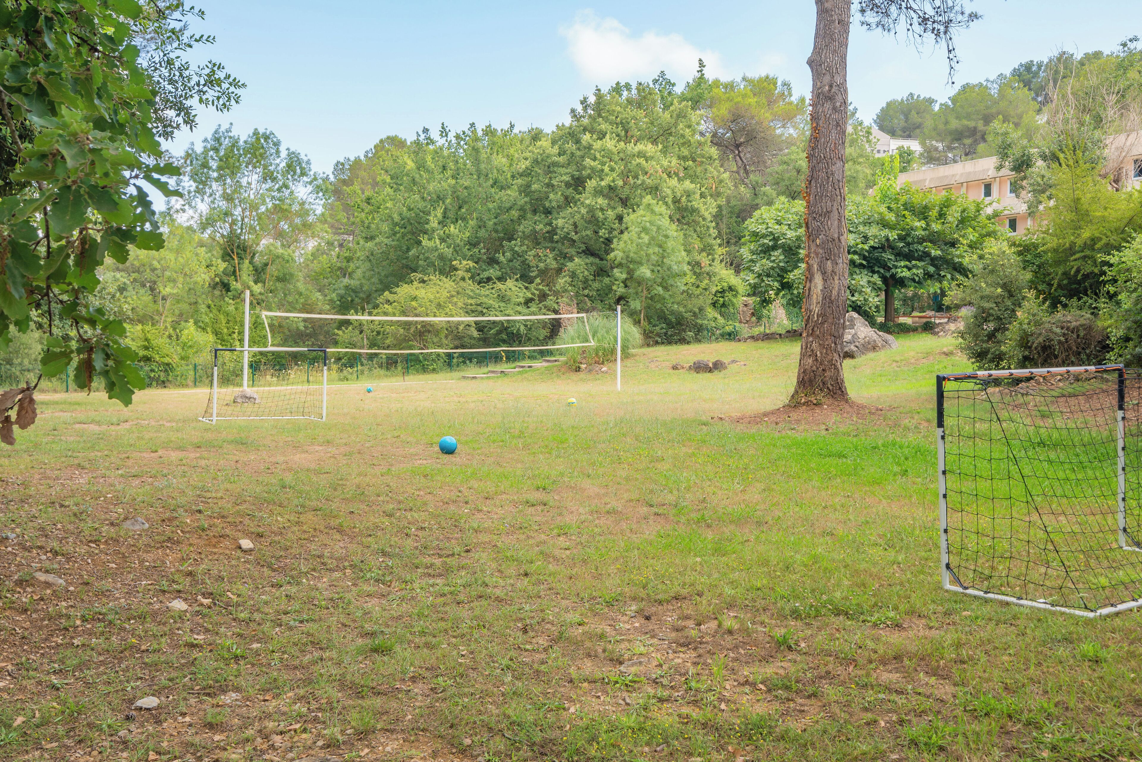 Un espace extérieur recouvert d’herbe, équipé d’un filet de volley-ball et d’un but de football.