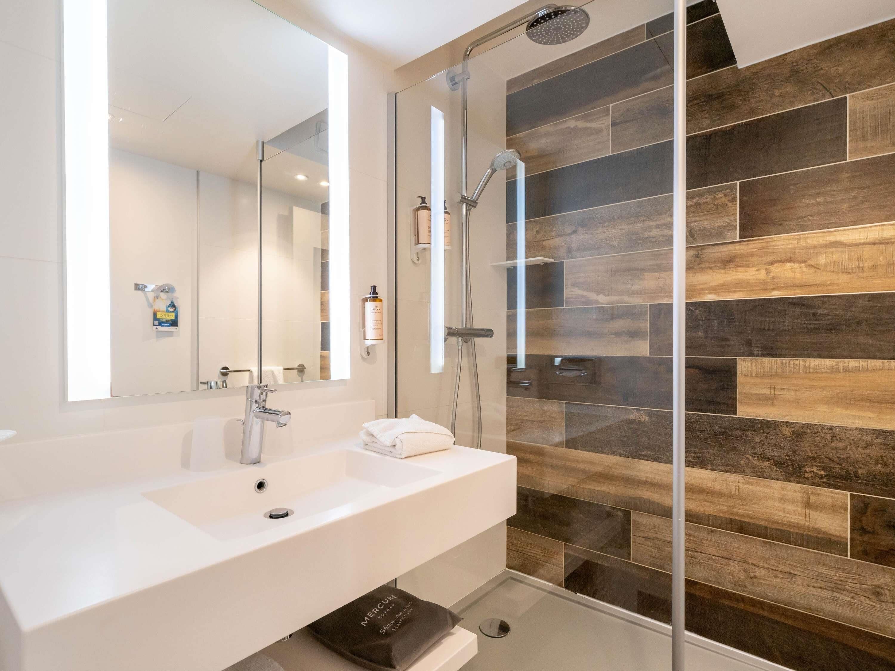 A modern bathroom with a large mirror, a sink, a shower, and a glass-enclosed shower area.
