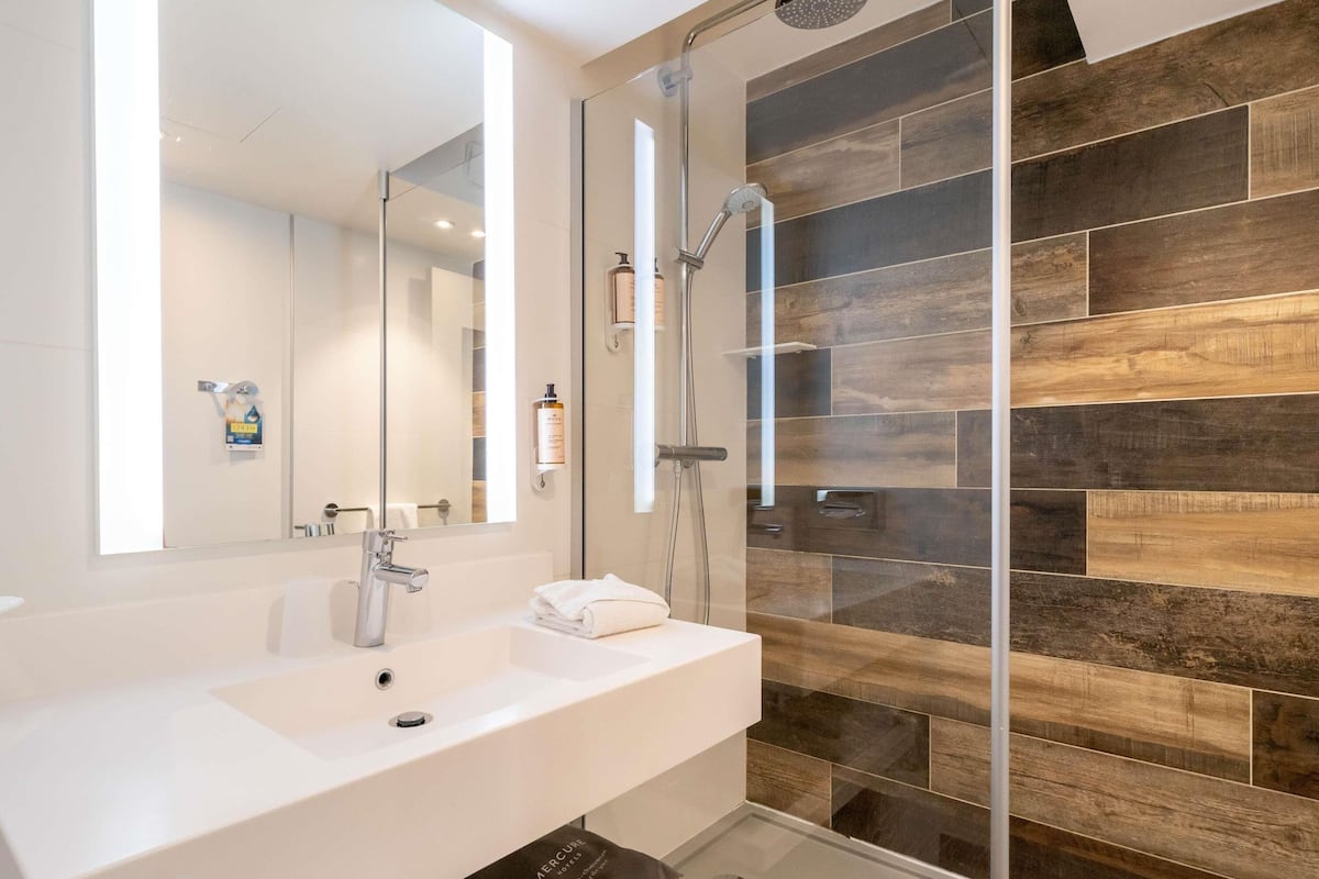 A modern bathroom with a large mirror, a sink, a shower, and a glass-enclosed shower area.