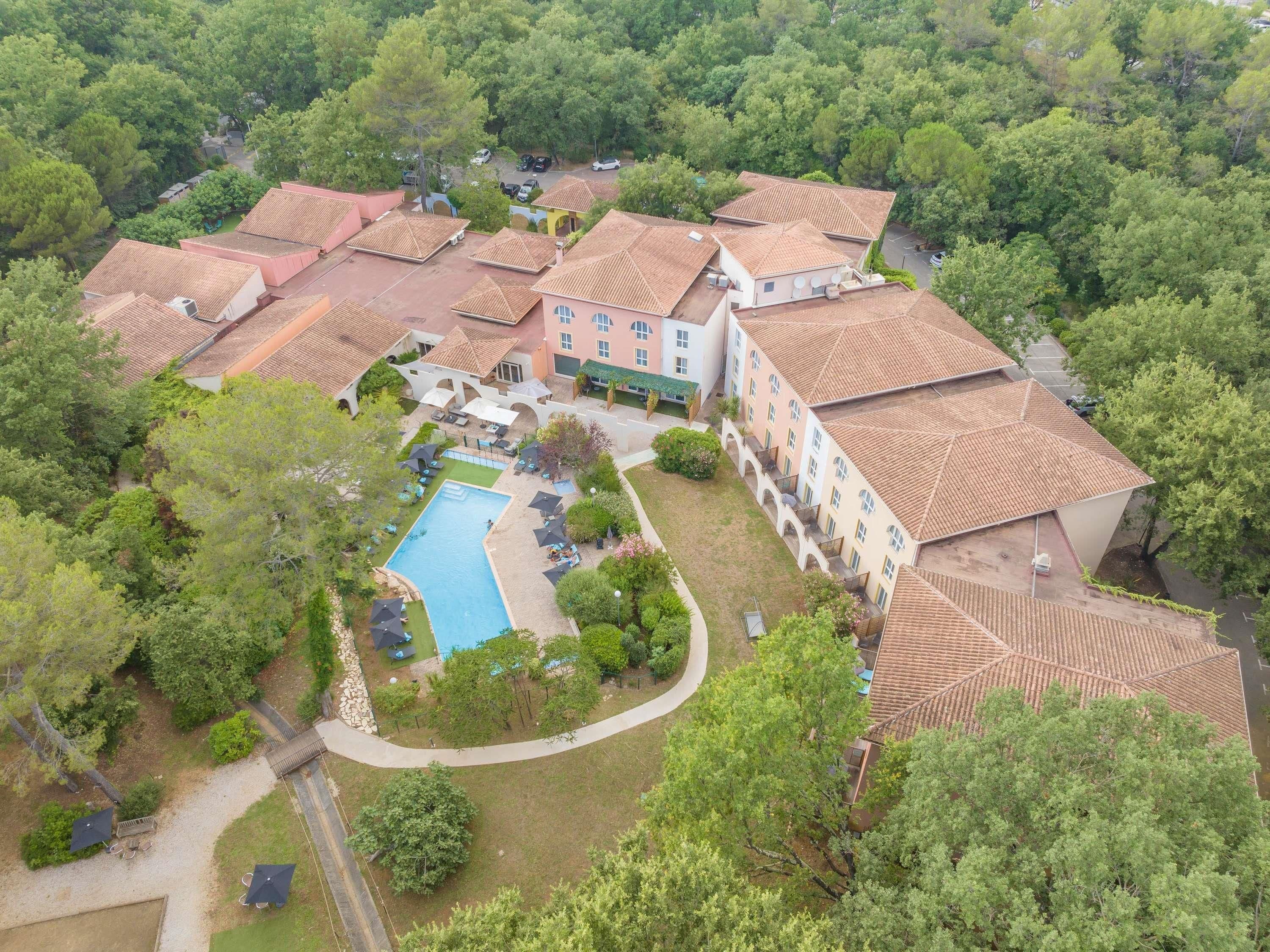 An aerial view of a hotel with multiple buildings, a swimming pool, and surrounding greenery.