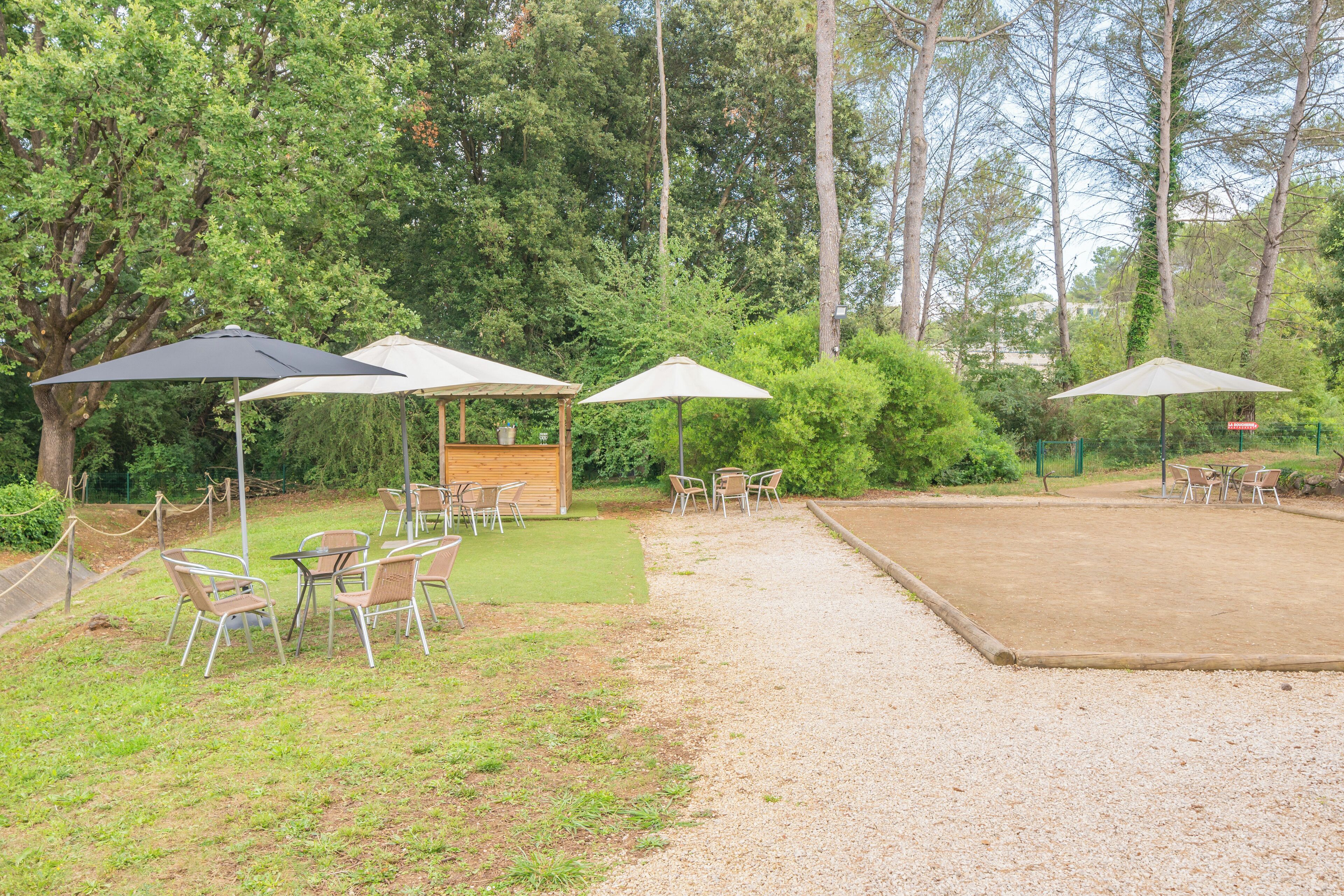 An outdoor seating area with tables and chairs under umbrellas, surrounded by trees.