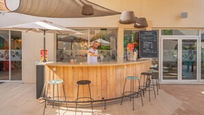 An outdoor bar area with a wooden counter, bar stools, and a menu board.