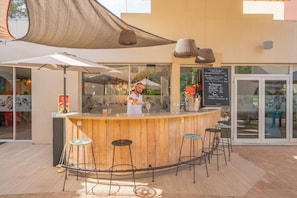 Un espace bar extérieur doté d’un comptoir en bois, de tabourets de bar et d’un tableau affichant le menu.
