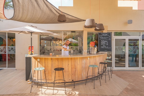Un espace bar extérieur doté d’un comptoir en bois, de tabourets de bar et d’un tableau affichant le menu.