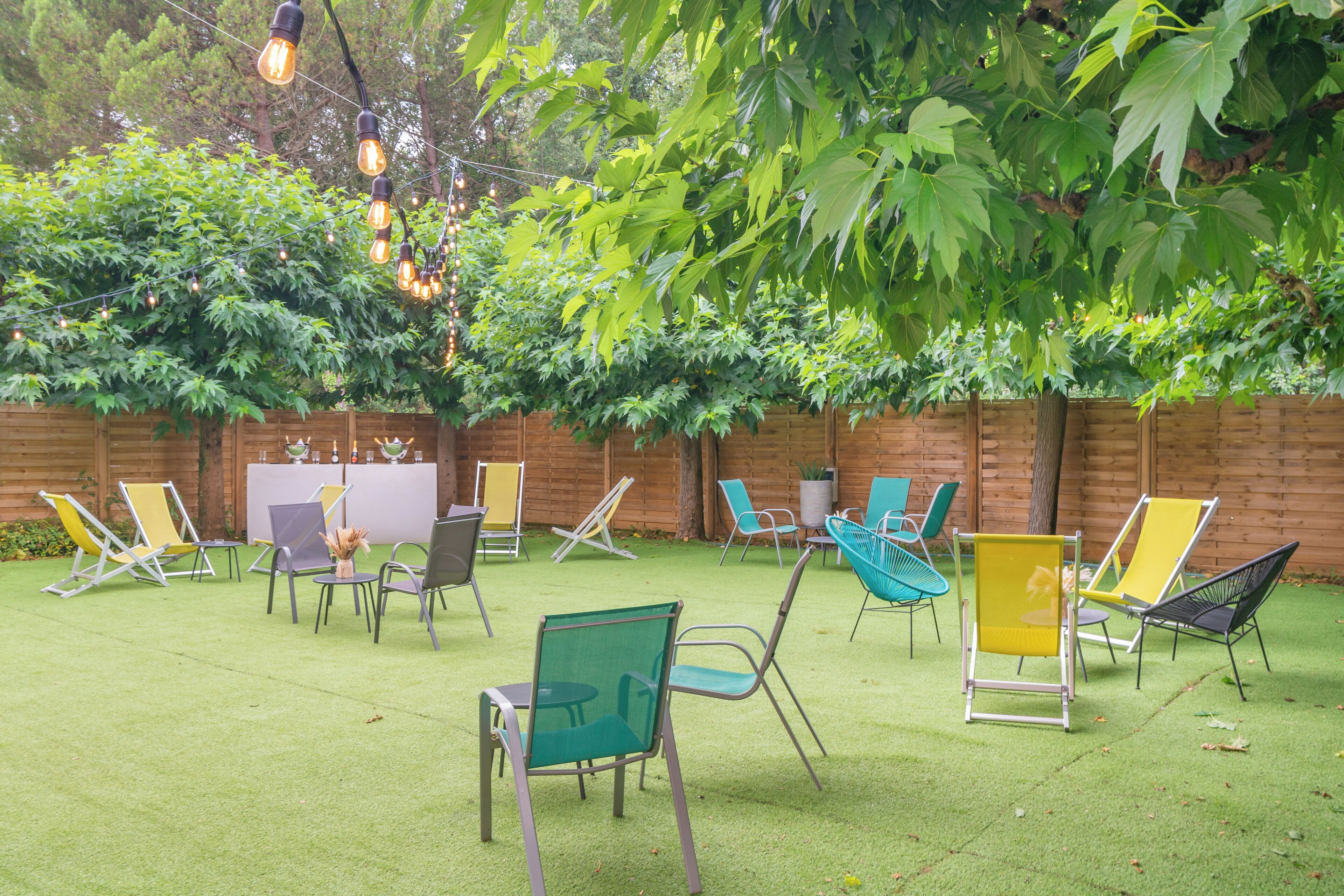 An outdoor seating area with multiple chairs and tables, surrounded by a wooden fence and greenery.