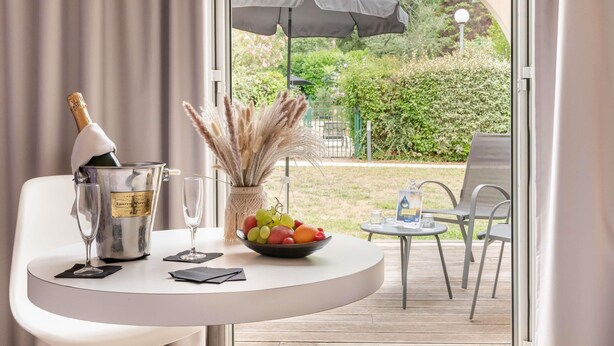 A table with a bottle of champagne, a glass, a bowl of fruit, and a vase with pampas grass.