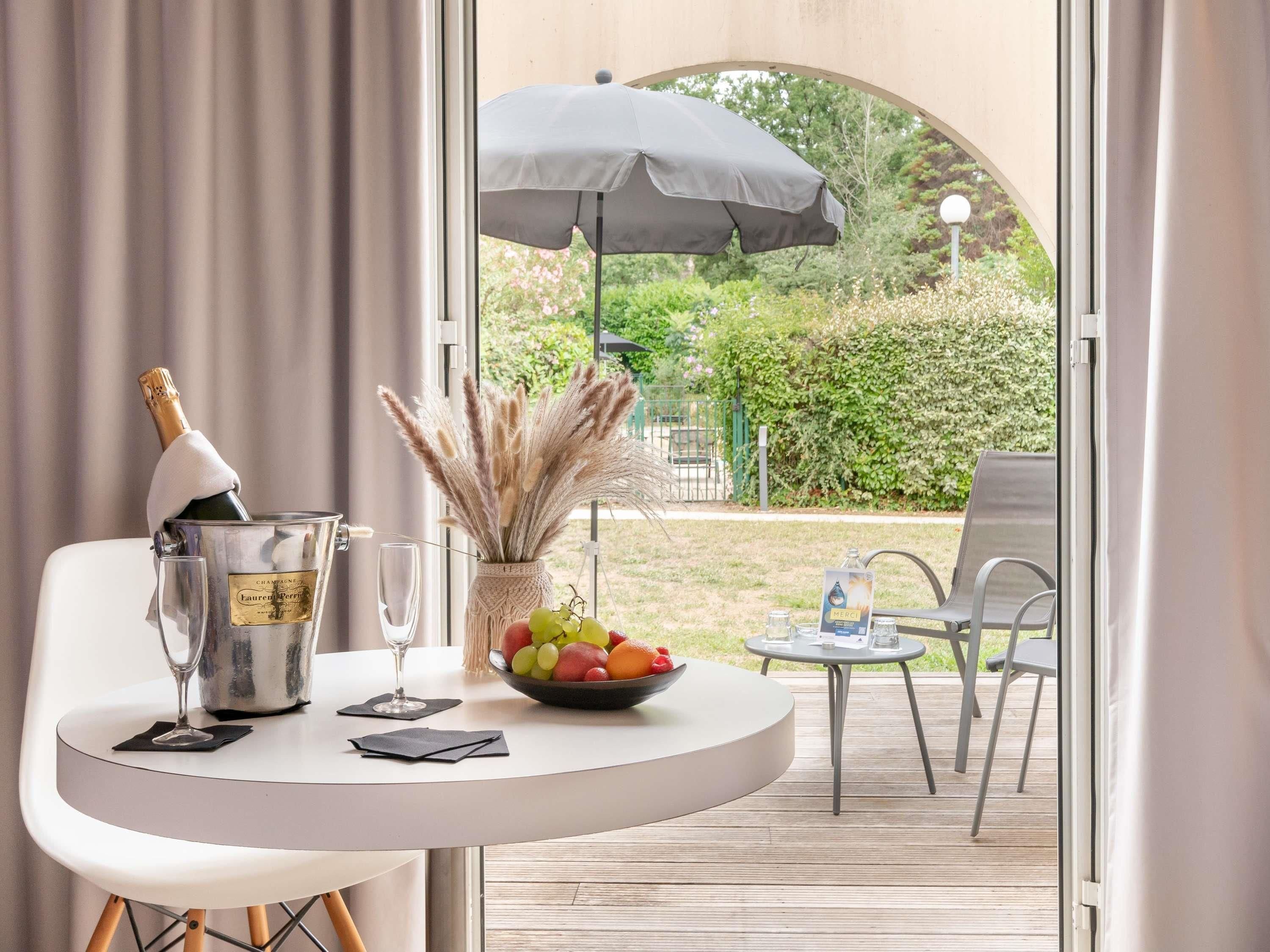 A table with a bottle of champagne, a glass, a bowl of fruit, and a vase with pampas grass.