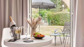 A table with a bottle of champagne, a glass, a bowl of fruit, and a vase with pampas grass.