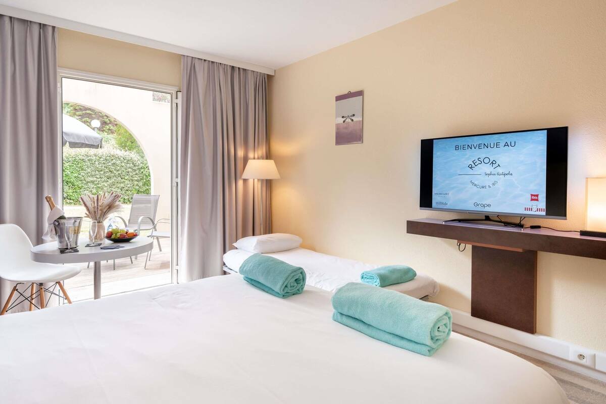 Ein Hotelzimmer mit Bett, Schreibtisch mit Stuhl, Fernseher und Blick ins Freie.