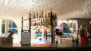 Un espace bar doté d’un plafond décoré de motifs de feuilles blanches, d’un présentoir pour les bouteilles et d’un présentoir à menus.