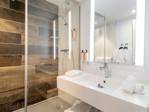 Une salle de bain moderne avec une douche à l’italienne en verre, un lavabo blanc et un grand miroir.