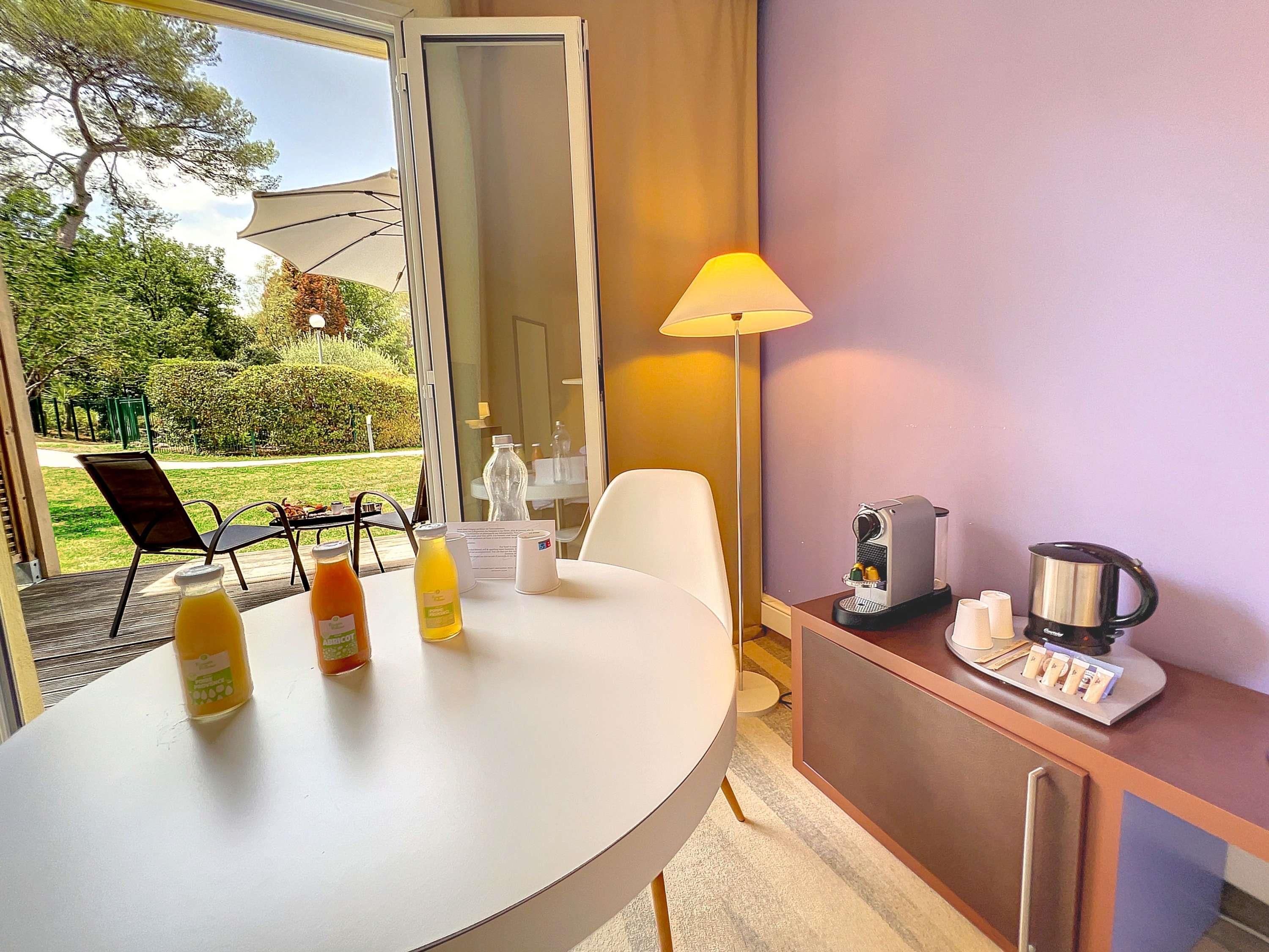 A hotel room with a round dining table, a coffee maker, a kettle, and a breakfast bar.