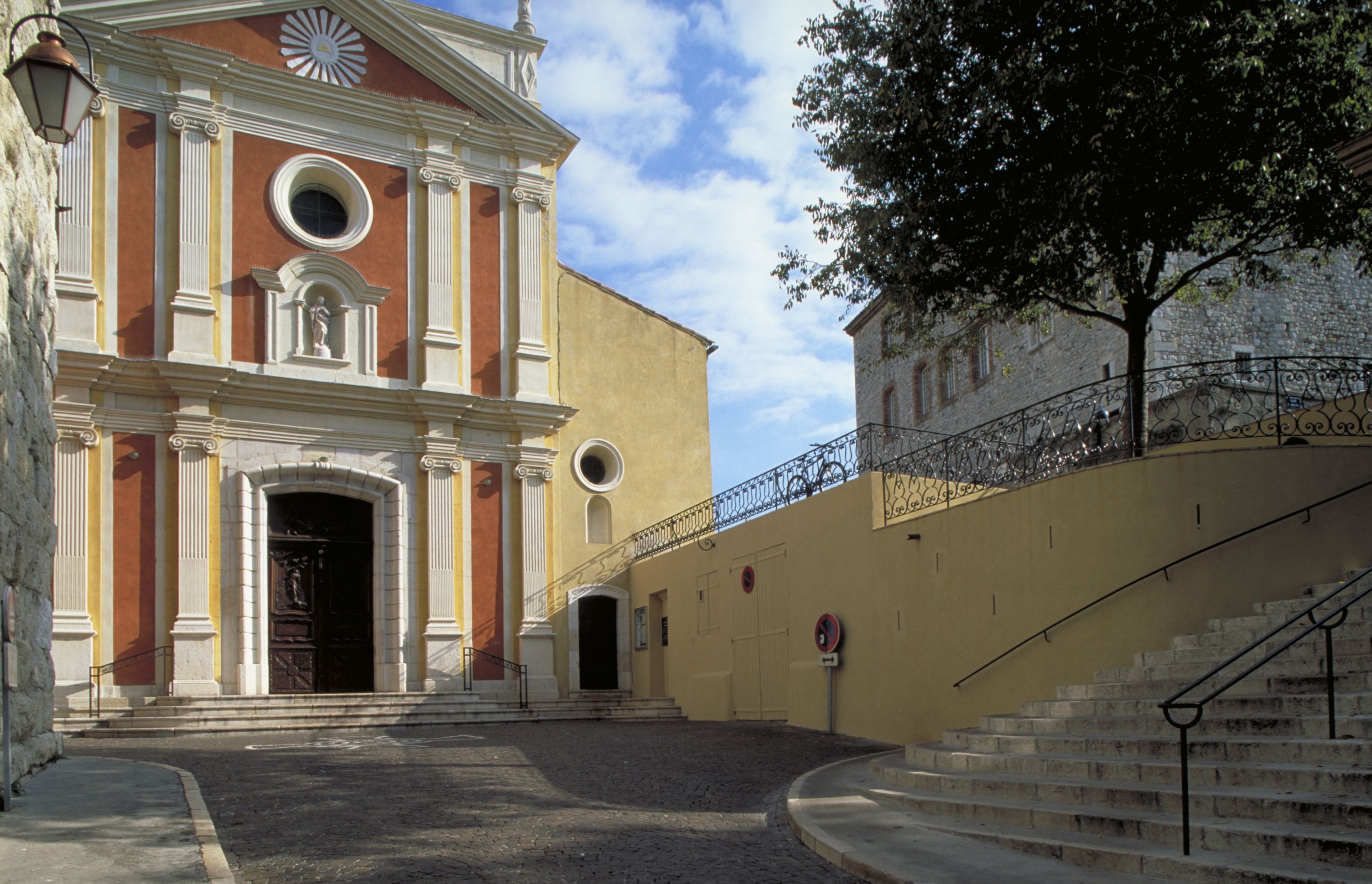 A building with a classical facade, a staircase, and a street in front.