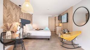 A modern hotel room with a bed, a dining table, a yellow rocking chair, a TV, and a mirror.
