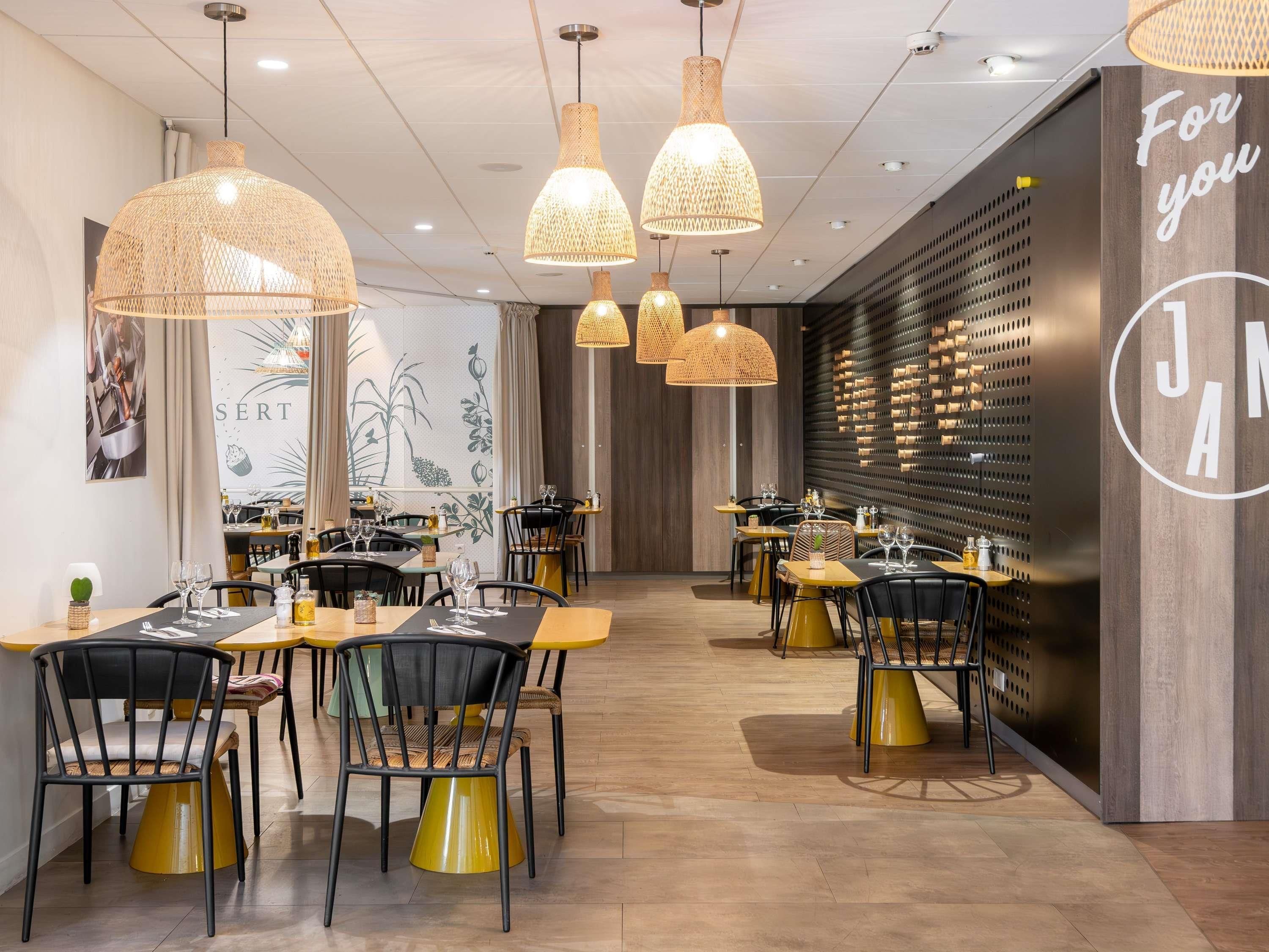 A modern restaurant interior with multiple dining tables, black and yellow chairs, and hanging wicker lamps.