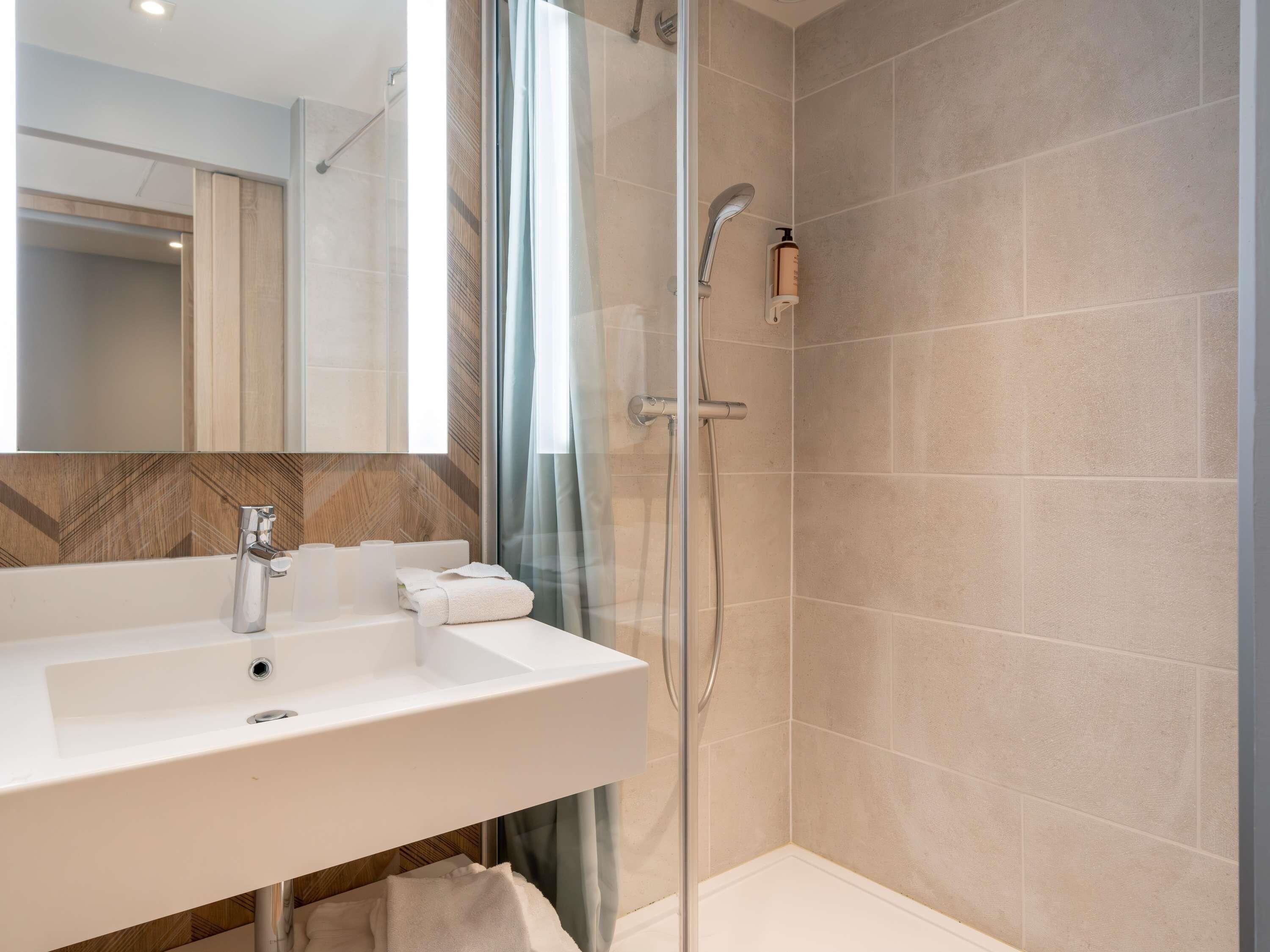 A modern bathroom with a white sink, a glass shower enclosure, and a mirror above the sink.