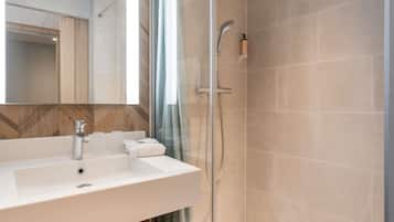 A modern bathroom with a white sink, a glass shower enclosure, and a mirror above the sink.