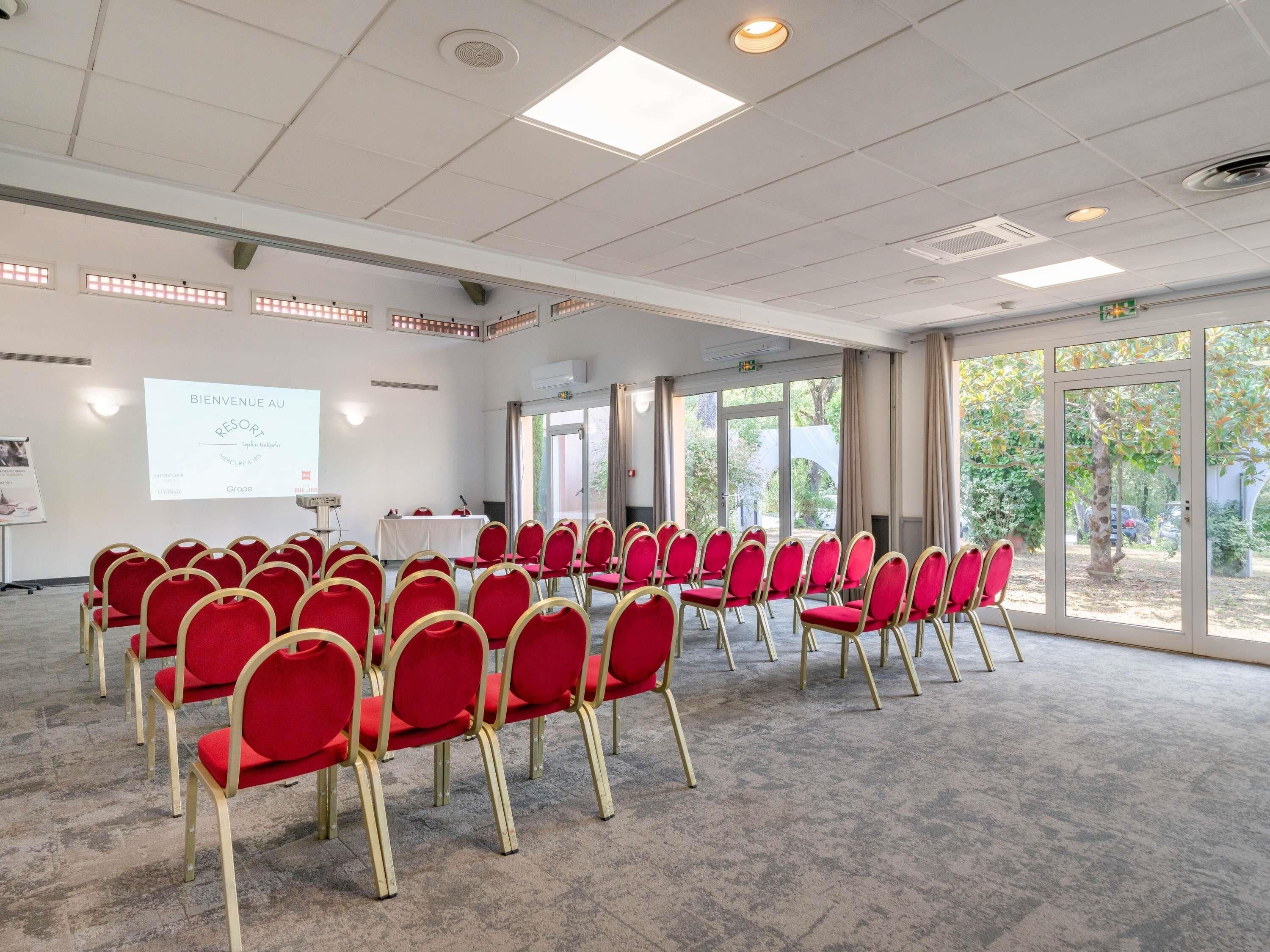 A conference room with rows of red chairs, a whiteboard, and a projector screen.