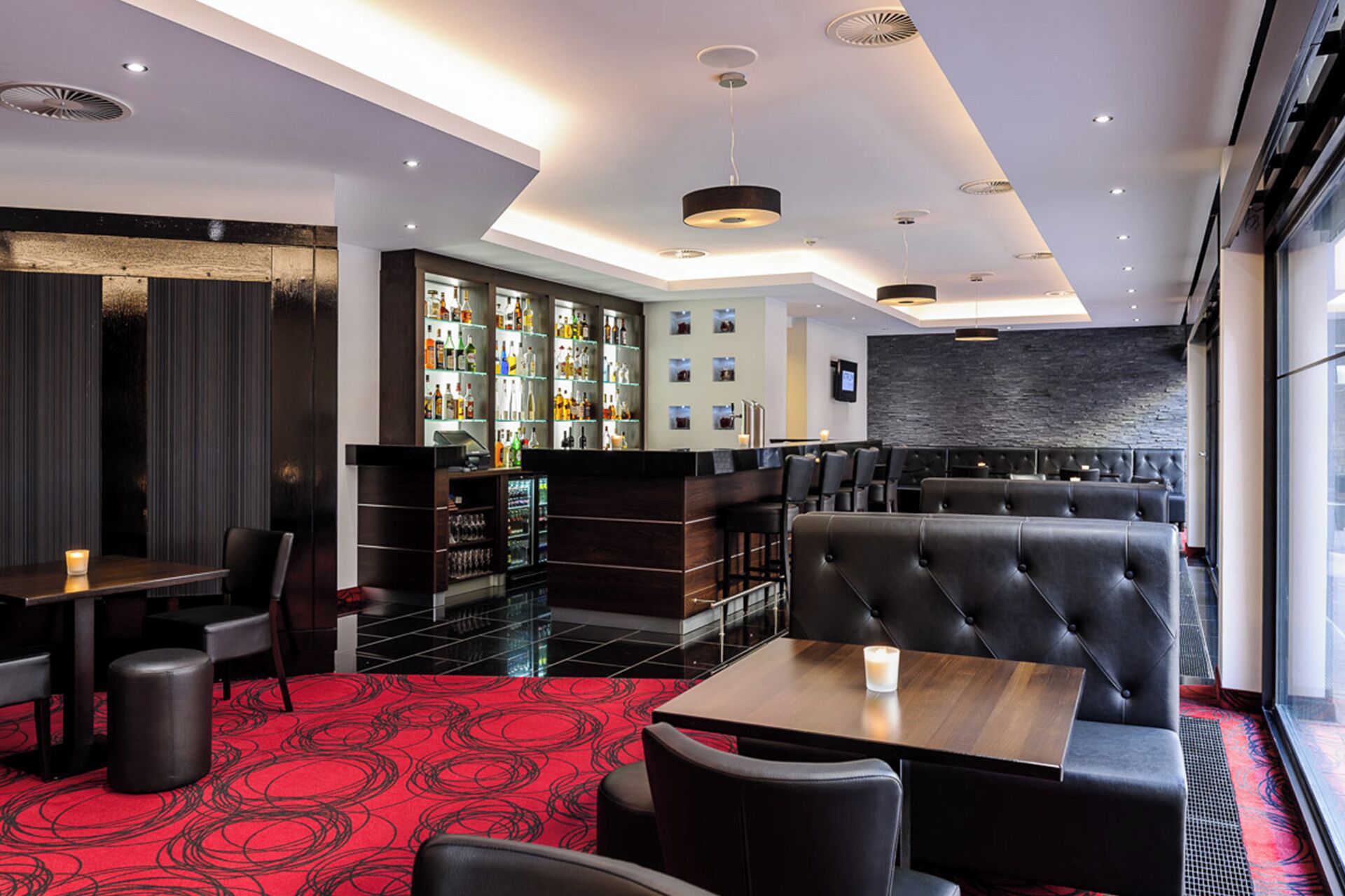 A modern bar area with leather seating, a bar counter, and a variety of liquor bottles.