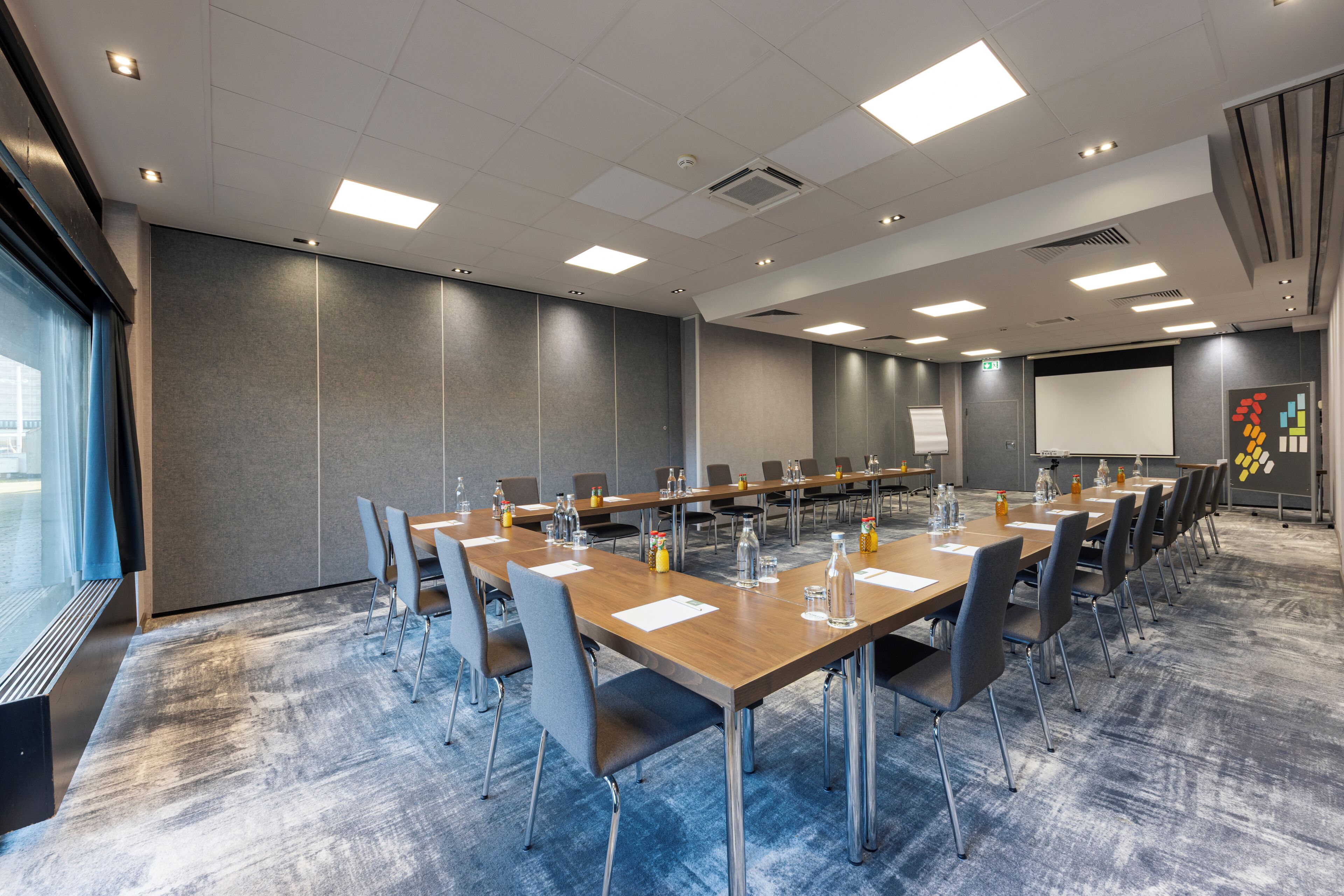 A conference room with long tables, chairs, and a projector screen.