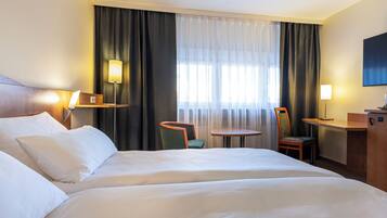Habitación de hotel con una cama grande, un escritorio, dos sillas, un televisor y una ventana con cortinas.