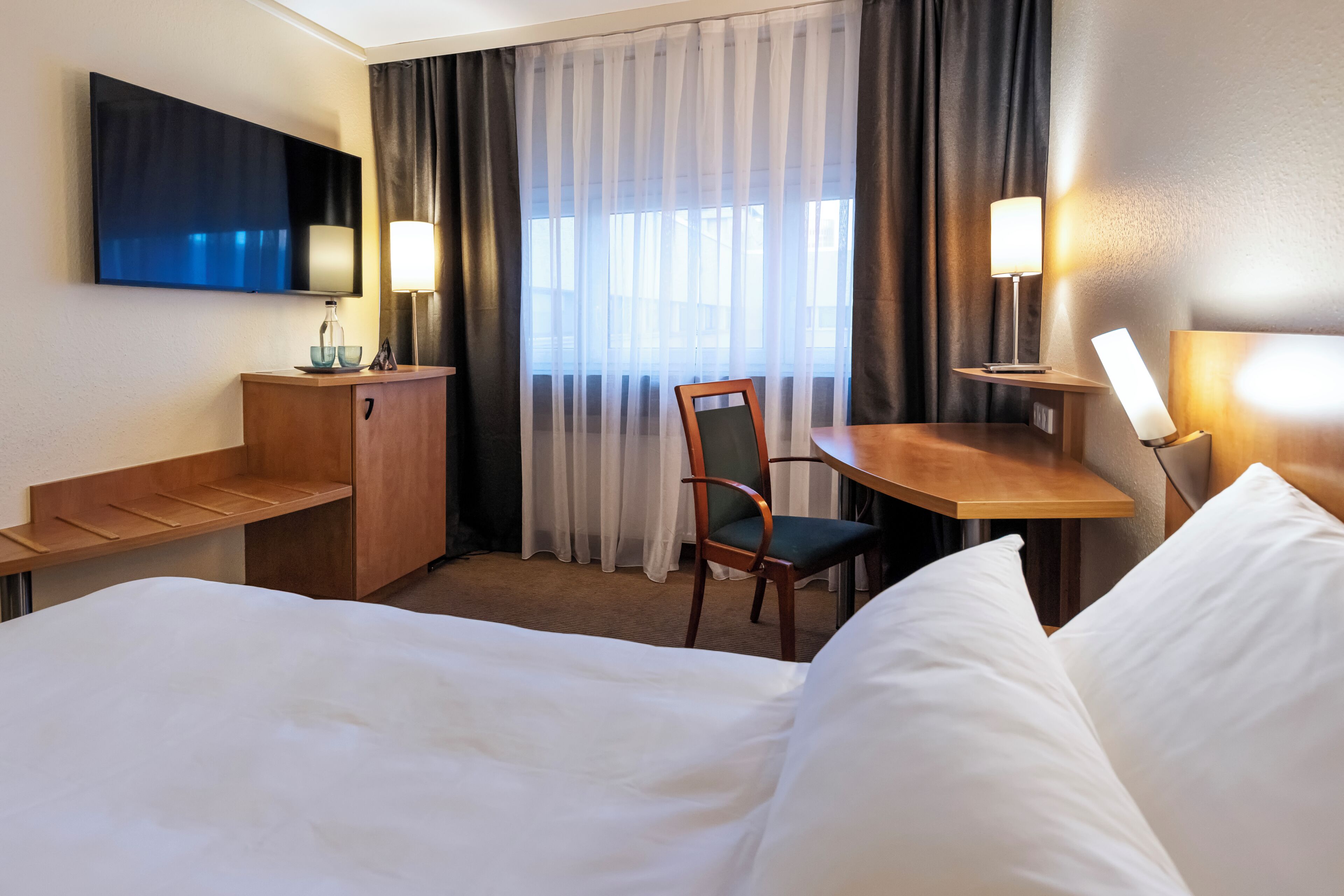 A hotel room with a bed, a desk, a chair, a television, and a window with curtains.
