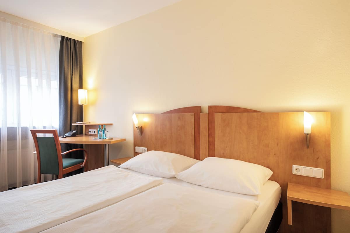 Une chambre d’hôtel avec un lit double, un bureau avec une chaise et deux tables de chevet avec des lampes.