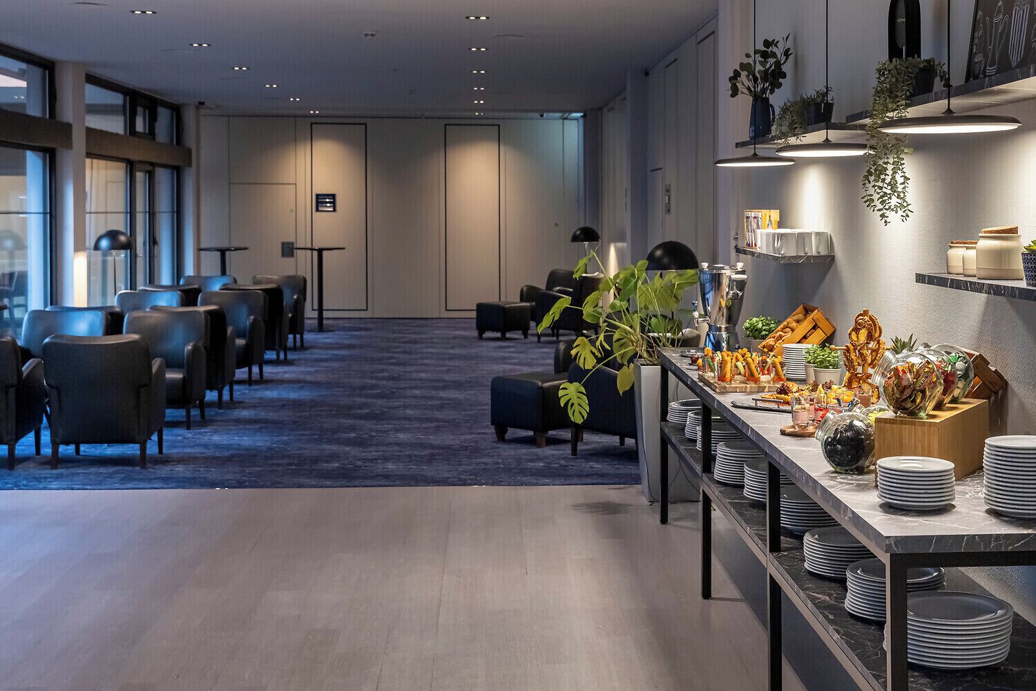 Un hall d’hôtel moderne avec un long comptoir d’accueil, un espace salon et un buffet.