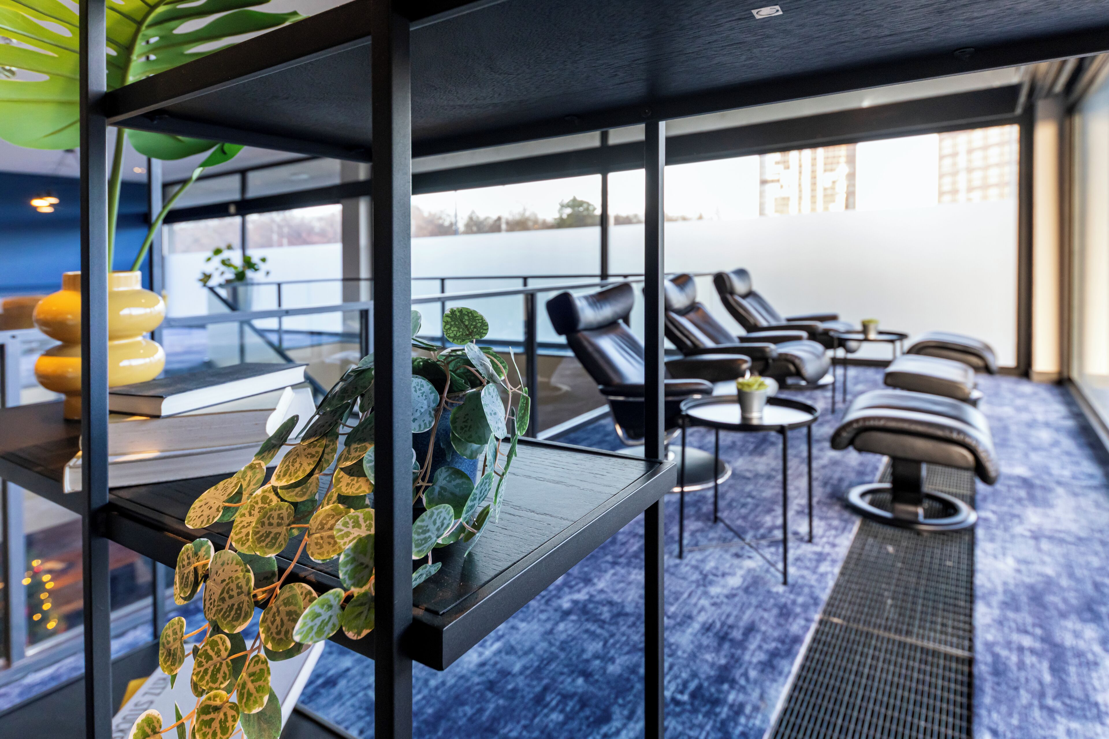 A modern lounge area with a view of a body of water, featuring a seating arrangement and a plant display.