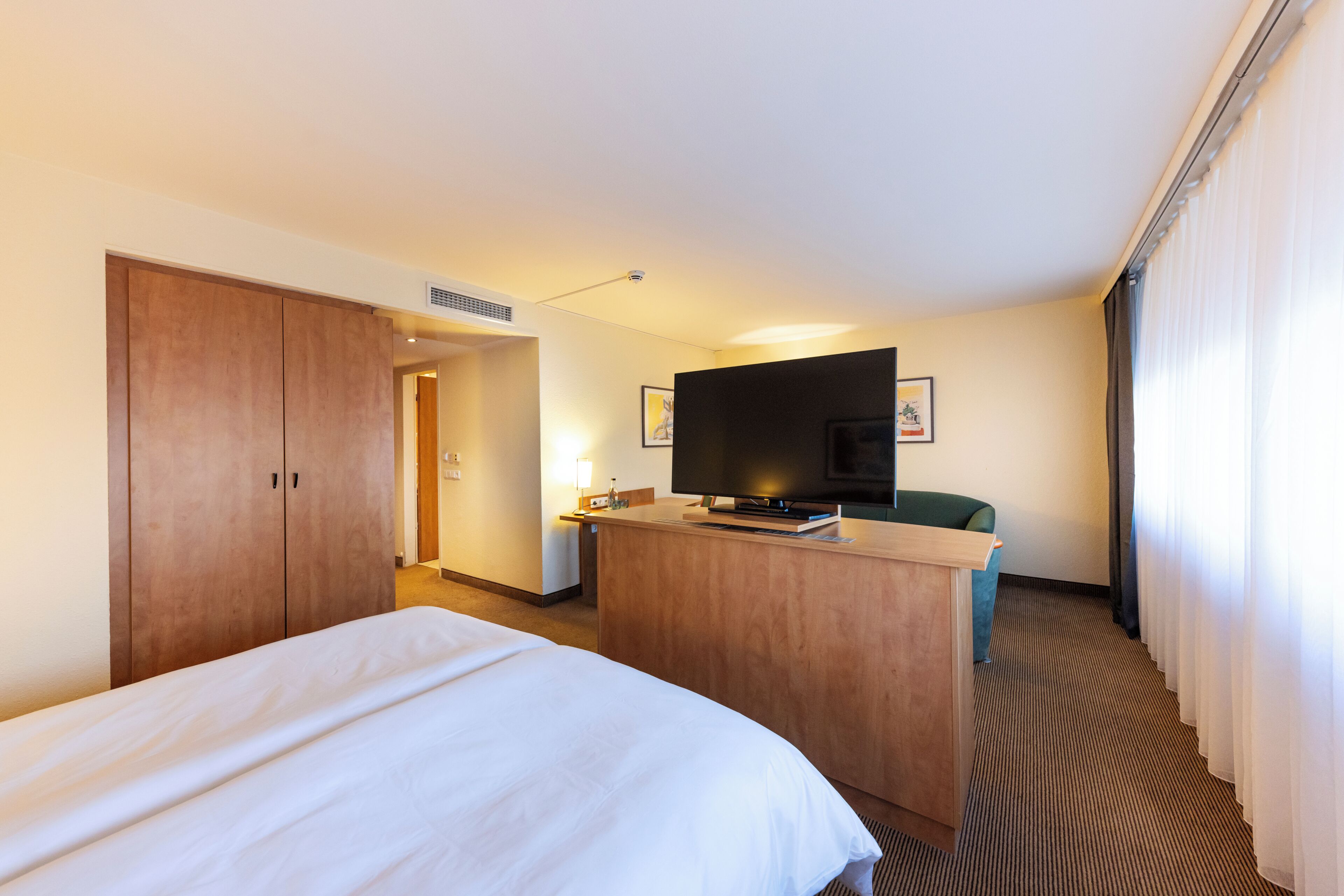 A hotel room with a bed, a desk with a television, and a door leading to another room.